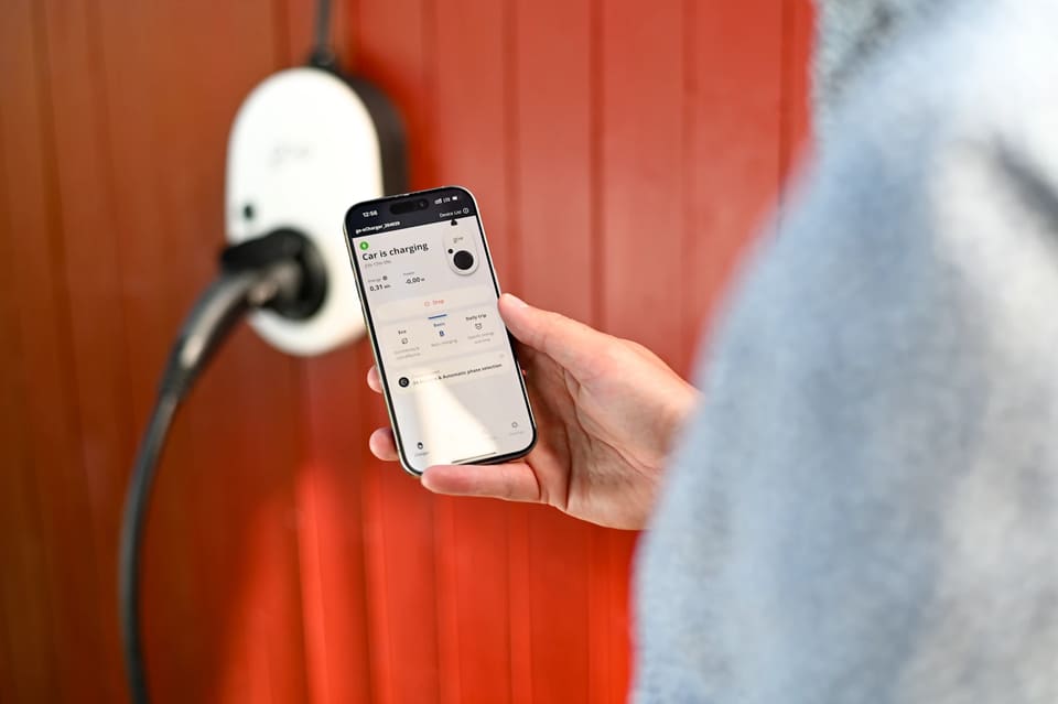 Una persona sigue en la app del móvil la carga desde un wallbox de pared con el cable conectado